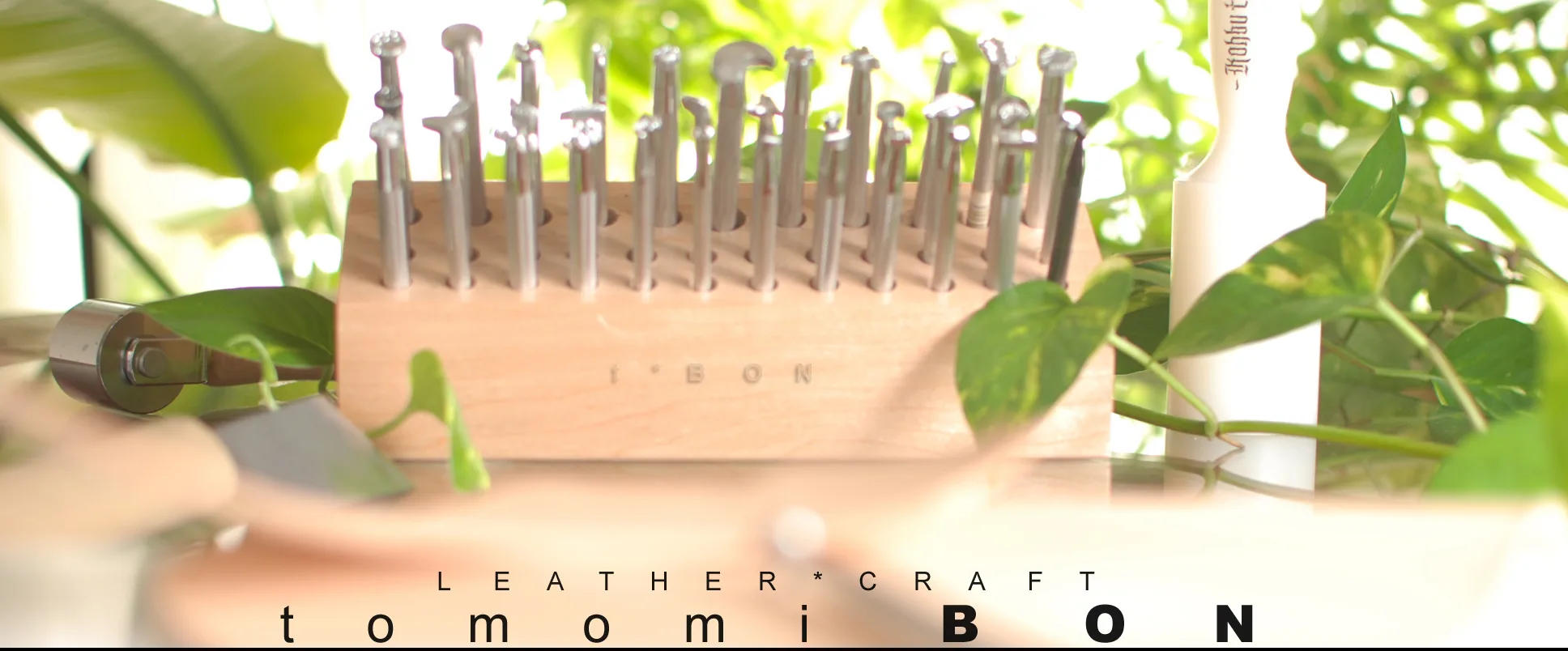 観葉植物に囲まれた作業台に、刻印用の打ち具や革包丁が並んでいる様子